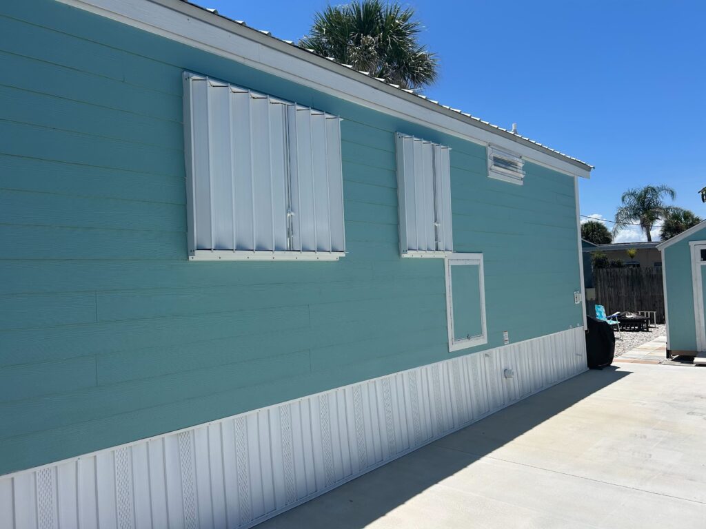 Turquoise blue mobile home with white accordion hurricane shutters in Melbourne Florida