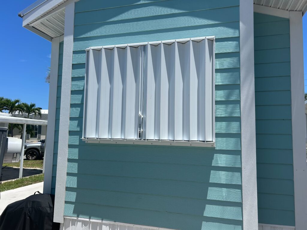 Front view of turquoise blue mobile home with white accordion hurricane shutters in Melbourne Florida